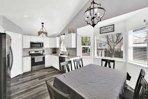 Kitchen featuring stainless steel appliances, white cabinets, vaulted ceiling, backsplash, and dark wood finished floors