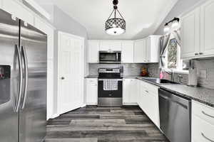 Kitchen featuring stainless steel appliances, lofted ceiling, white cabinetry, and decorative backsplash