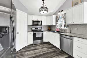 Kitchen with stainless steel appliances, white cabinets, light stone counters, dark wood-type flooring, and vaulted ceiling