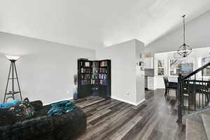 Living area featuring dark wood-style flooring, hanging lights, and vaulted ceiling