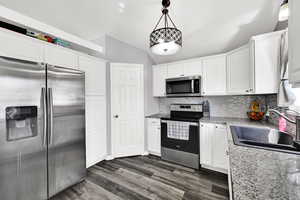 Kitchen with stainless steel appliances, white cabinets, backsplash, vaulted ceiling, and dark wood-style floors
