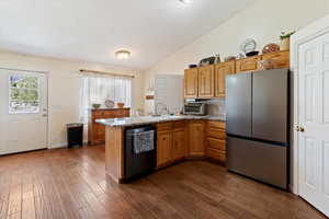 Kitchen featuring lofted ceiling, freestanding refrigerator, dishwasher, a peninsula, and dark wood finished floors
