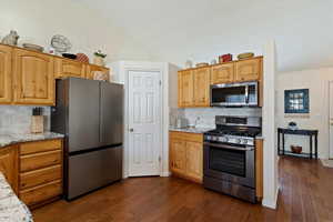 Kitchen with stainless steel appliances, light stone countertops, dark wood-style floors, decorative backsplash, and lofted ceiling
