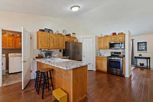 Kitchen featuring stainless steel appliances, decorative backsplash, dark wood finished floors, light stone counters, and lofted ceiling