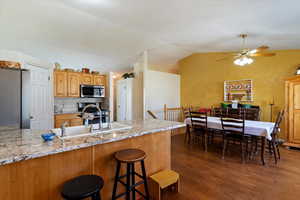 Kitchen with stainless steel appliances, dark wood-type flooring, a breakfast bar, tasteful backsplash, and light stone countertops