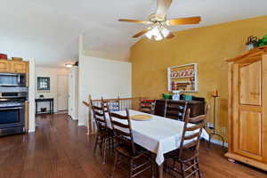 Dining room with dark wood finished floors, vaulted ceiling, and ceiling fan
