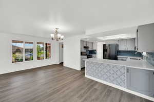Kitchen with a peninsula, stainless steel appliances, a chandelier, gray cabinetry, and light wood finished floors