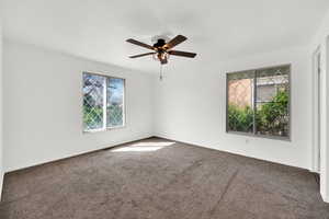 Unfurnished room with dark colored carpet and ceiling fan