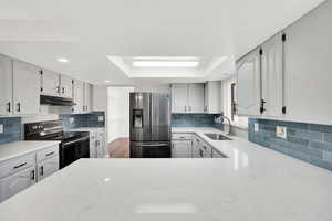 Kitchen featuring electric range, stainless steel fridge, a tray ceiling, white cabinetry, and light stone countertops