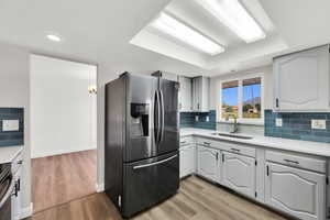 Kitchen featuring stainless steel fridge with ice dispenser, light wood-style floors, brick wall, light stone countertops, and tasteful backsplash