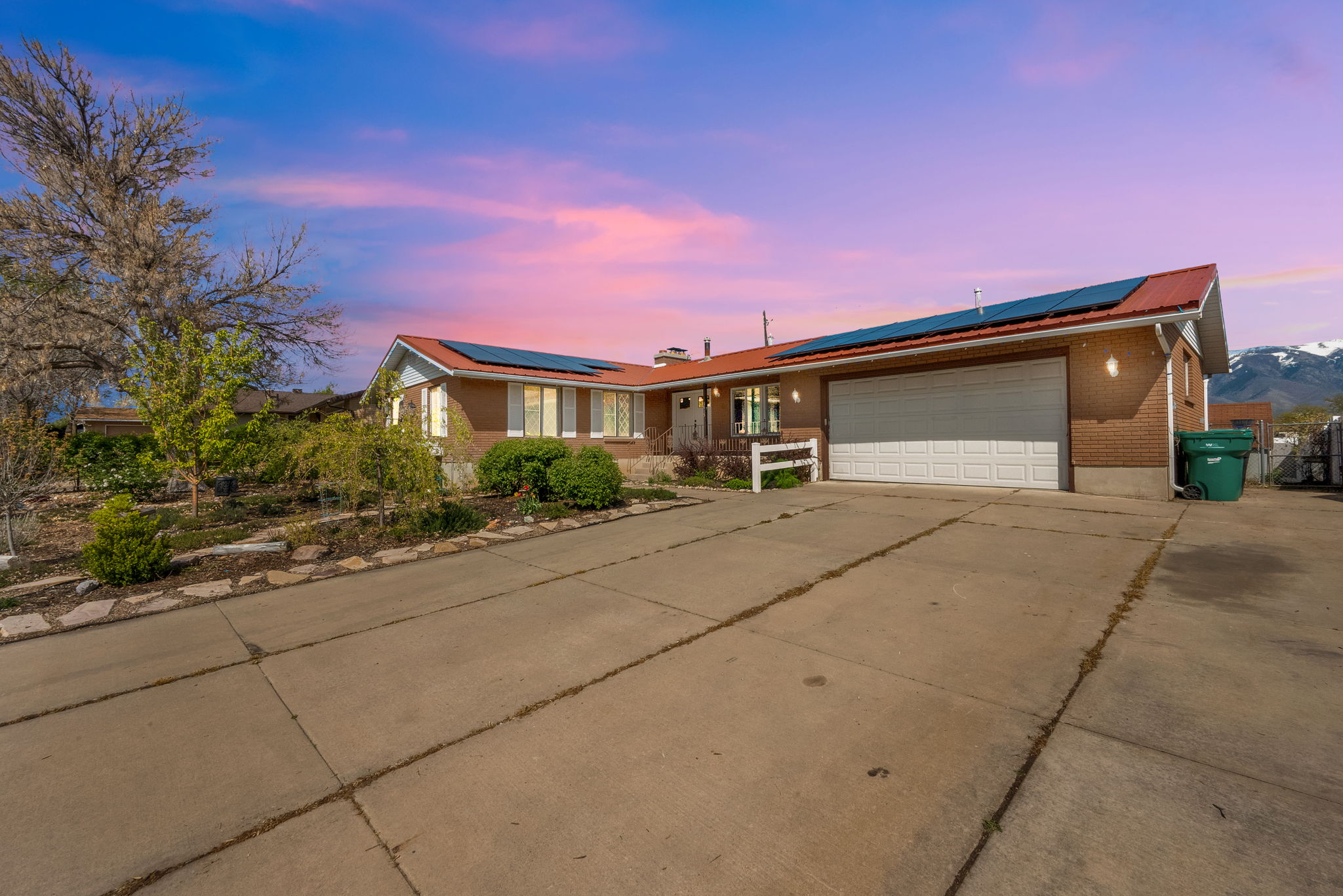 Ranch-style house with roof mounted solar panels, driveway, a garage, and a metal roof