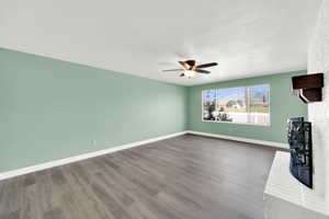 Unfurnished living room with a fireplace, dark wood-type flooring, and ceiling fan