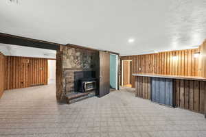 Unfurnished living room featuring wooden walls, light carpet, a wood stove, a textured ceiling, and bar