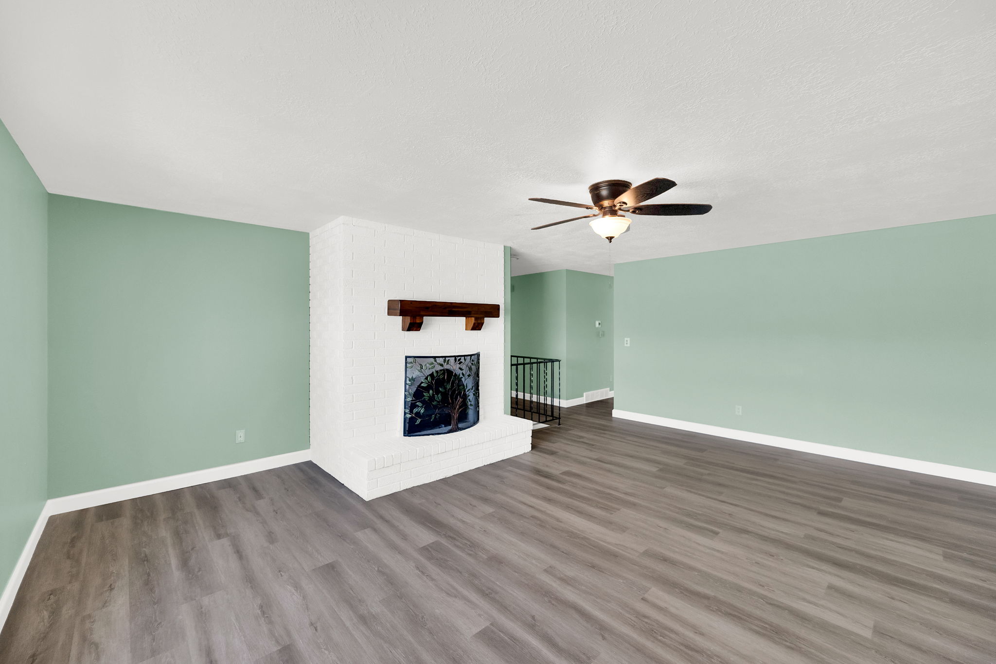 Unfurnished living room featuring a brick fireplace, a ceiling fan, dark wood finished floors, and a textured ceiling