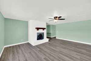Unfurnished living room featuring a brick fireplace, a ceiling fan, dark wood finished floors, and a textured ceiling