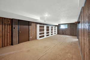 Basement featuring a textured ceiling, wooden walls, and carpet floors