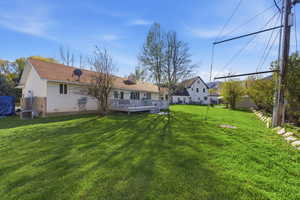 Back of property featuring a deck, a lawn, brick siding, a chimney, and stucco siding