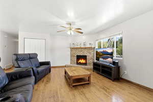 Living room with a brick fireplace, a ceiling fan, and light wood-style flooring