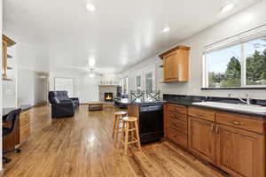 Kitchen with a breakfast bar area, a brick fireplace, open floor plan, light wood-style floors, and dishwasher