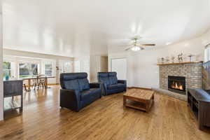 Living room featuring a brick fireplace, wood finished floors, and ceiling fan