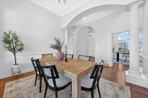 Dining area with ornate columns, dark wood-style floors, suspended lighting, arched walkways, and crown molding