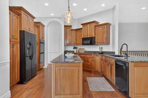 Kitchen featuring dark stone countertops, a peninsula, black appliances, and dark wood-style flooring