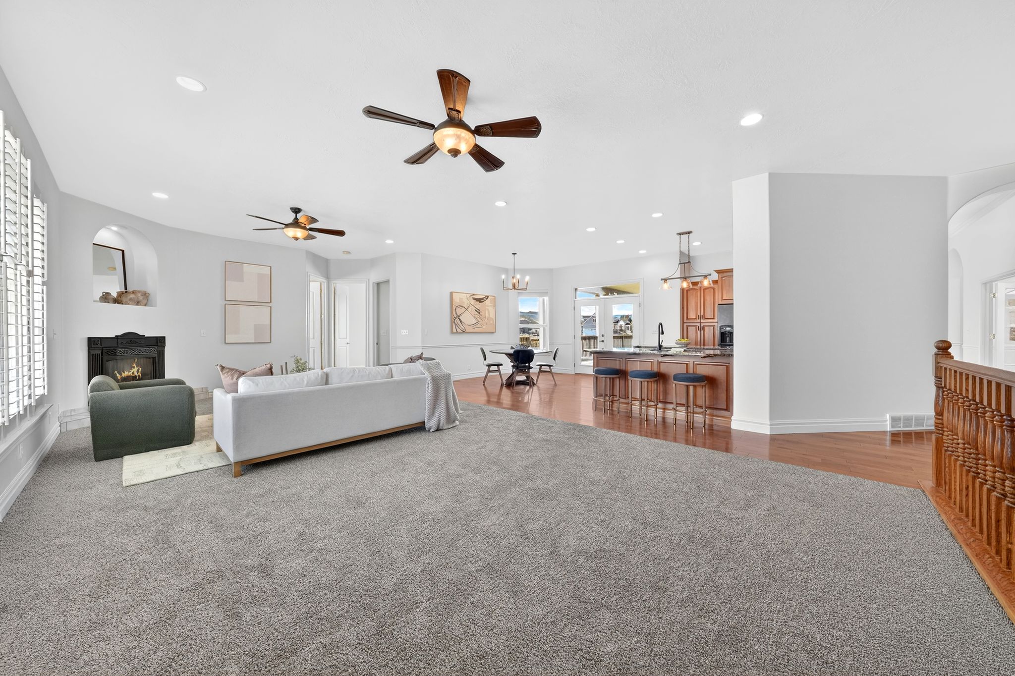 Living room with arched walkways, a warm lit fireplace, ceiling fan, dark carpet, and a chandelier
