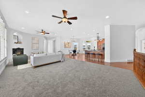 Living room with arched walkways, a warm lit fireplace, ceiling fan, dark carpet, and a chandelier