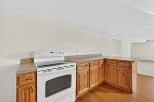 Kitchen featuring electric stove, a peninsula, light wood-style floors, and a textured ceiling
