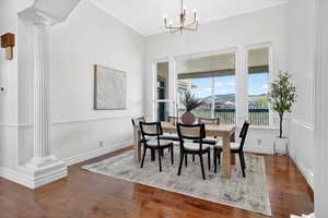 Dining area featuring dark wood-style floors, decorative columns, crown molding, hanging lights, and a mountain view