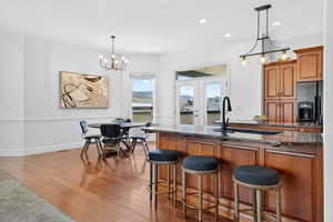 Kitchen with dark stone counters, a breakfast bar, wood finish cabinetry, dark wood-style floors, and black fridge