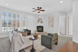 Carpeted living area featuring a ceiling fan, recessed lighting, a glass covered fireplace, and hardwood / wood-style floors
