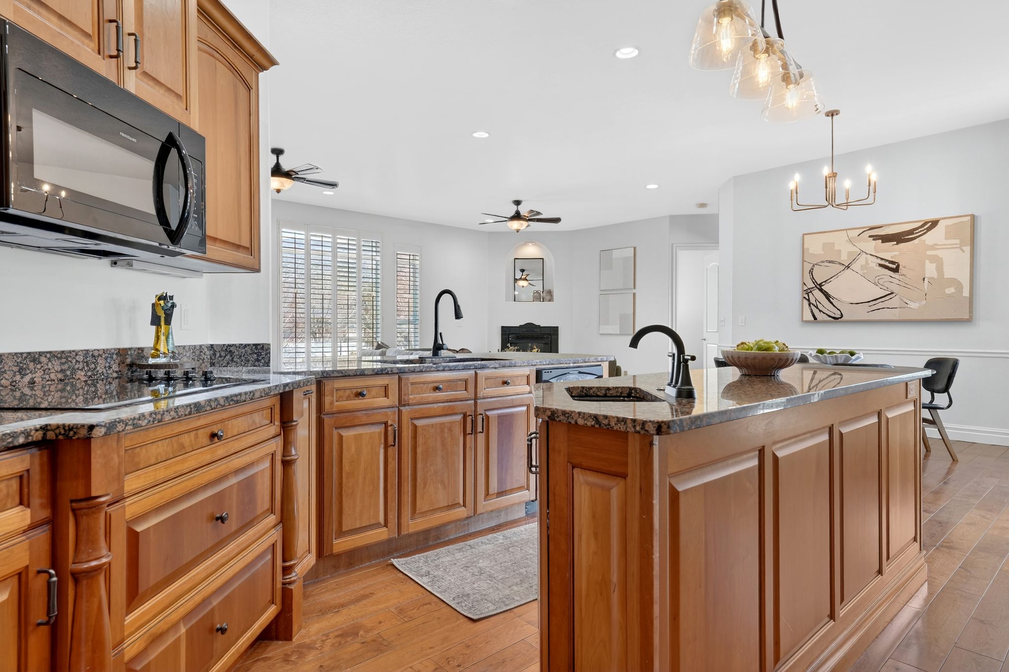 Kitchen with light wood-style flooring, black appliances, a peninsula, dark stone counters, and a warm lit fireplace