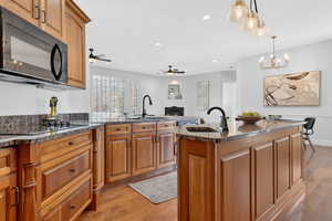 Kitchen with light wood-style flooring, black appliances, a peninsula, dark stone counters, and a warm lit fireplace