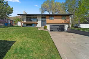 View of front facade with driveway, a chimney, a garage, a balcony, and stucco siding
