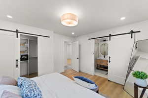Bedroom featuring a barn door, a spacious closet, light wood-style floors, ensuite bathroom, and recessed lighting
