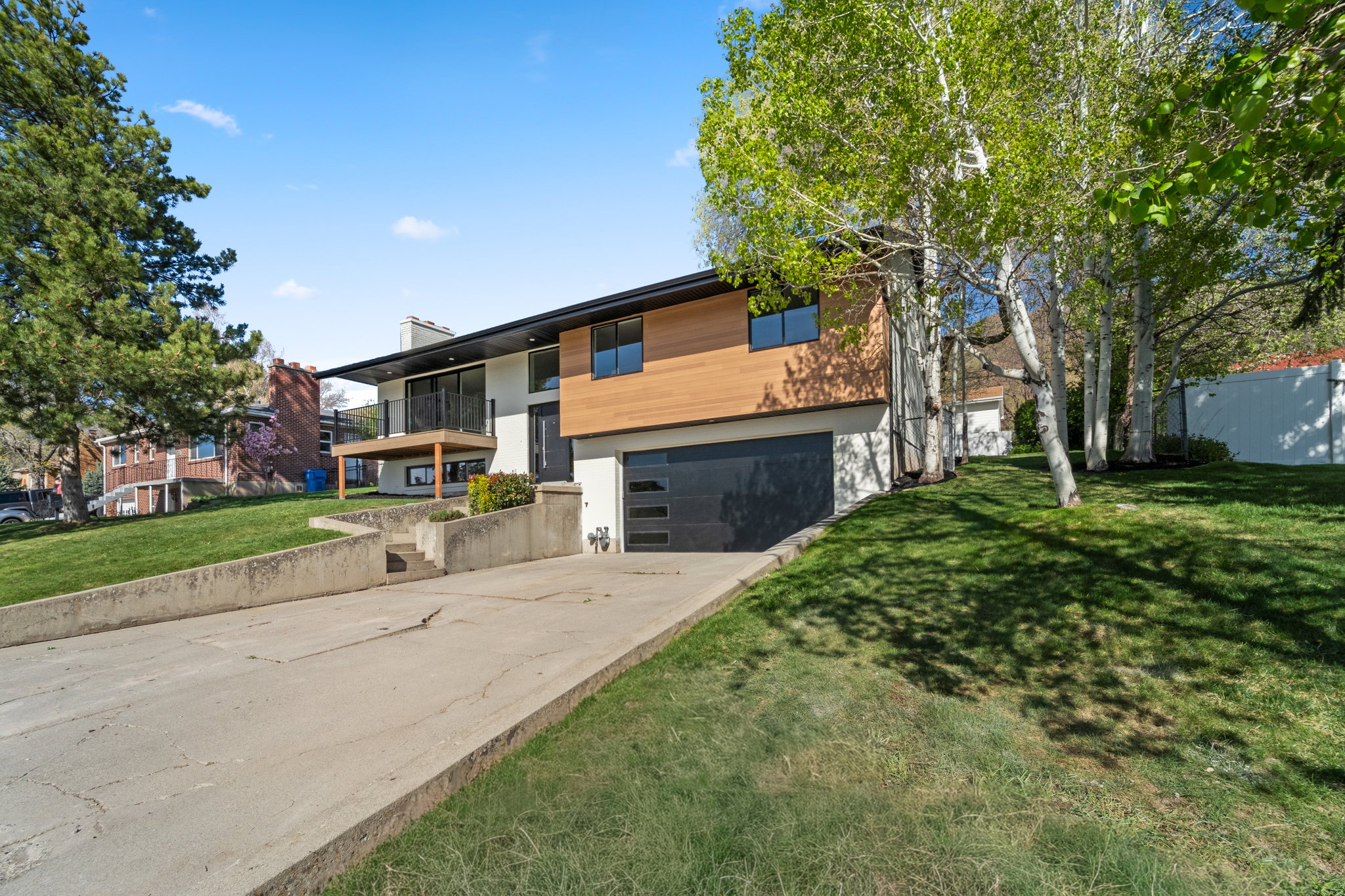 Contemporary house featuring a balcony, concrete driveway, an attached garage, a front yard, and a chimney