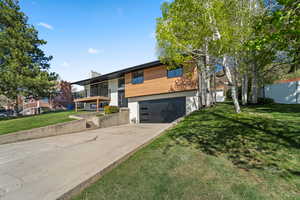Contemporary house featuring a balcony, concrete driveway, an attached garage, a front yard, and a chimney