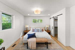 Bedroom featuring a spacious closet, a barn door, light wood-type flooring, recessed lighting, and a textured ceiling