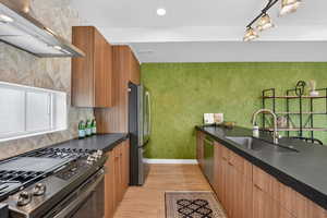Kitchen featuring stainless steel appliances, ventilation hood, light wood-style floors, backsplash, and wood finish cabinets