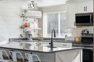 Kitchen featuring white cabinetry, range with electric cooktop, stainless steel microwave, dark stone countertops, and a kitchen breakfast bar