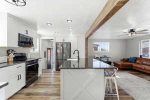 Kitchen with a breakfast bar area, dark stone countertops, electric range, white cabinetry, and freestanding refrigerator
