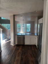 Kitchen featuring white cabinetry, dishwasher, dark wood finished floors, freestanding refrigerator, and decorative light fixtures
