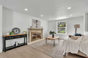 Living room with light wood-type flooring, a glass covered fireplace, and recessed lighting