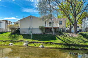 Rear view of property featuring a deck with water view and a lawn