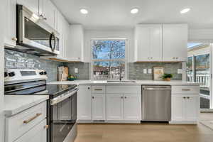 Kitchen featuring stainless steel appliances, white cabinetry, light wood-style flooring, light stone counters, and recessed lighting