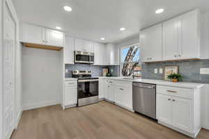 Kitchen featuring stainless steel appliances, white cabinets, light wood-style flooring, recessed lighting, and backsplash