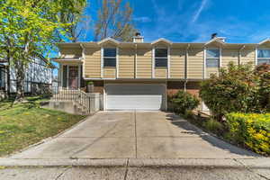 Split foyer home featuring a chimney, an attached garage, concrete driveway, and brick siding