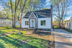 View of front of home featuring a chimney, stone siding, a shingled roof, and concrete driveway
