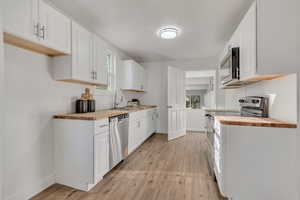 Kitchen with butcher block countertops, stainless steel appliances, white cabinetry, and light wood-style floors
